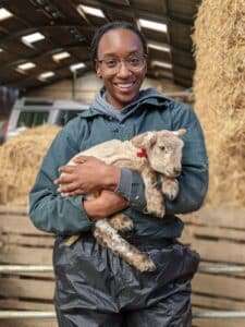Image of Remi in green overalls, smiling, holding a Lamb.