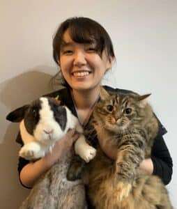 Image of Yui smiling, holding a grey and white Rabbit & long haired Tabby Cat.